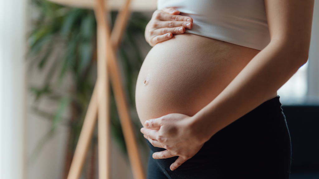 Nærbillede af en gravid mave, der illustrerer ro, støtte og velvære gennem graviditet og den første tid med småbørn.